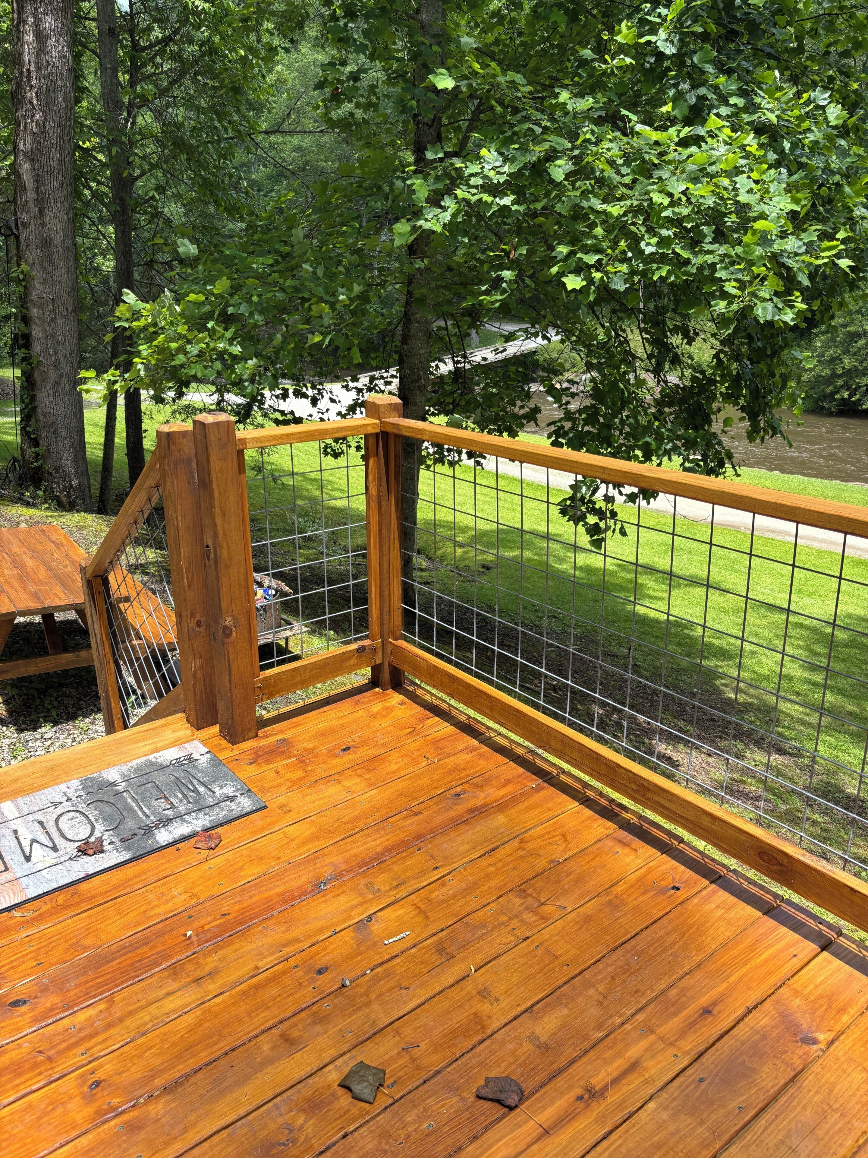 Una terraza de madera con una valla metálica, rodeada de árboles y un césped.