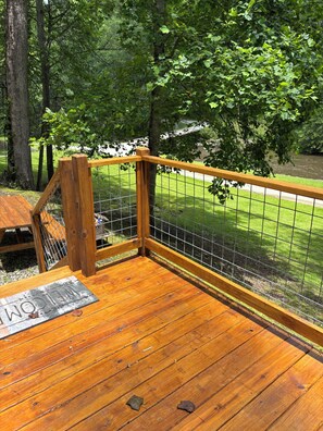 A wooden deck with a metal fence, surrounded by trees and a grassy area.