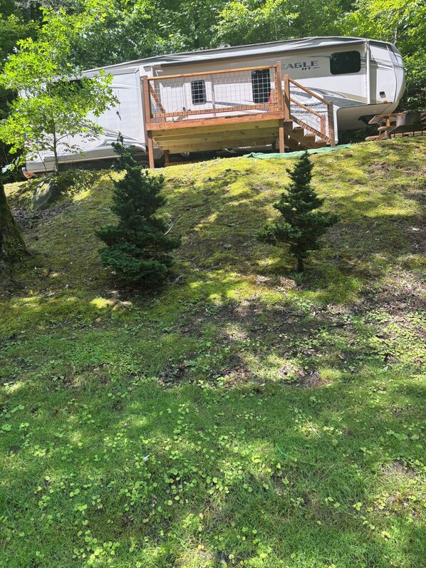 A recreational vehicle with a wooden deck and a ramp leading to a covered area.