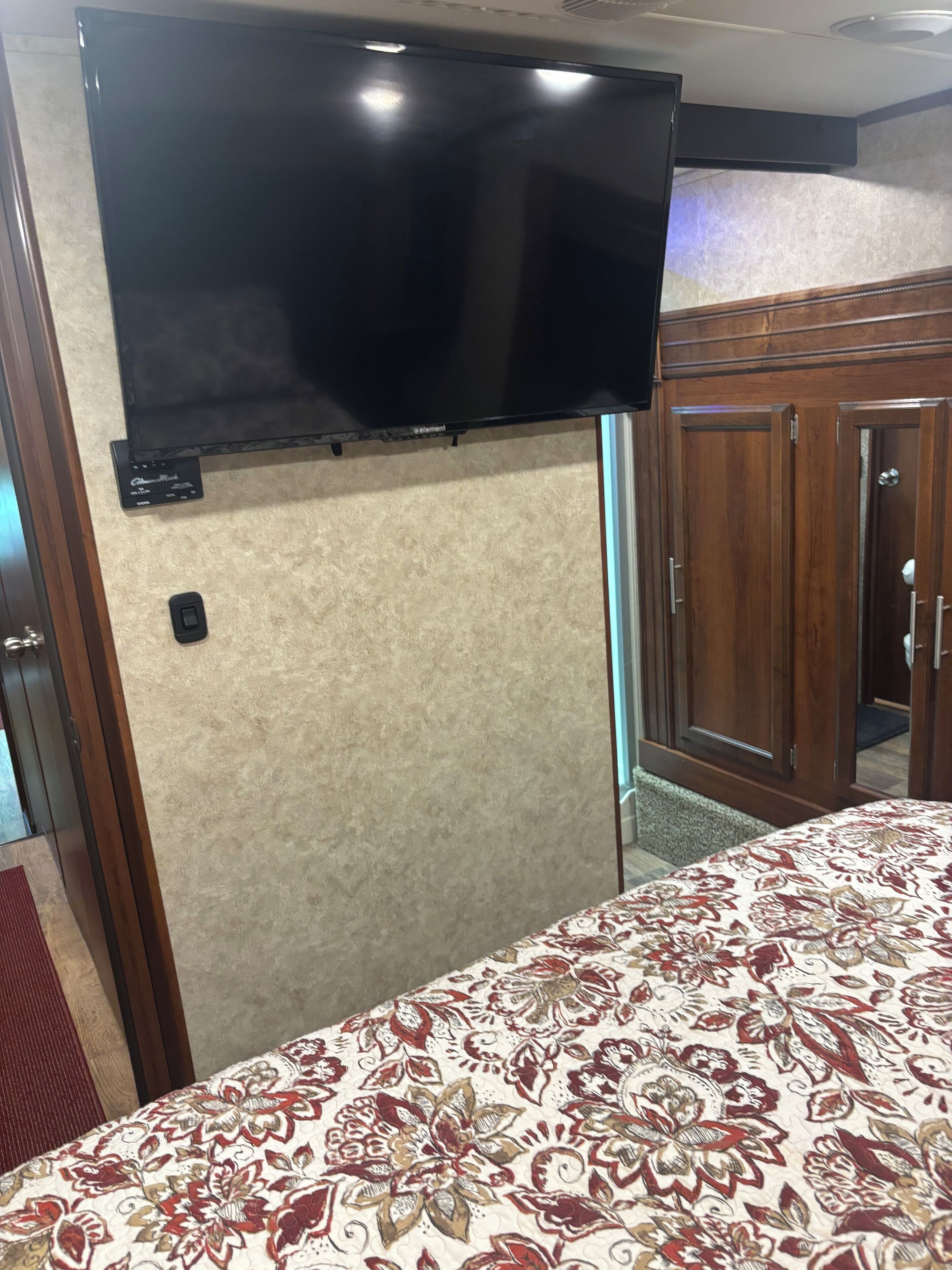 A room with a bed, a flat-screen TV mounted on the wall, and a wooden wardrobe.