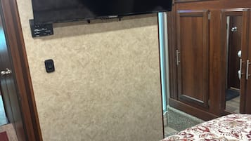 A room with a bed, a flat-screen TV mounted on the wall, and a wooden wardrobe.
