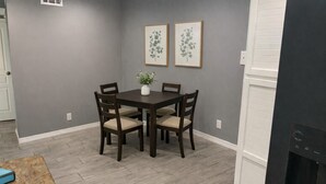Un comedor con una mesa y sillas de madera oscura, un jarrón con planta y dos láminas botánicas enmarcadas en la pared.