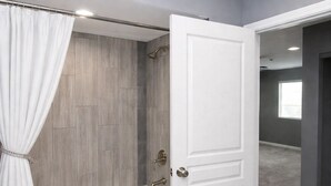 Un baño moderno con bañera, ducha y una puerta blanca que da a otra habitación.