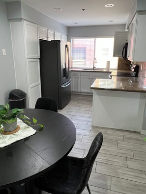 A modern kitchen with white cabinets, a black refrigerator, and a dining area with a table and chairs. - Sun Devil at 5th & Mill - ASU, Mill Ave & Spring Training (Tempe)
