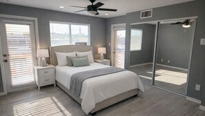 Un dormitorio con cama, mesitas de noche, lámparas, ventilador de techo y un espejo grande.