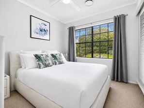 Ein Schlafzimmer mit einem großen Bett, einem Fenster mit Vorhängen, einem Heizkörper und einem gerahmten Bild an der Wand.