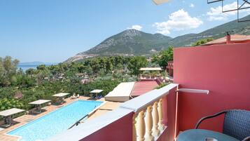 Un balcón con piscina, una mesa y vistas al mar y a las montañas.