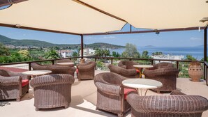 Área de estar externa com móveis de vime e vista para o mar.