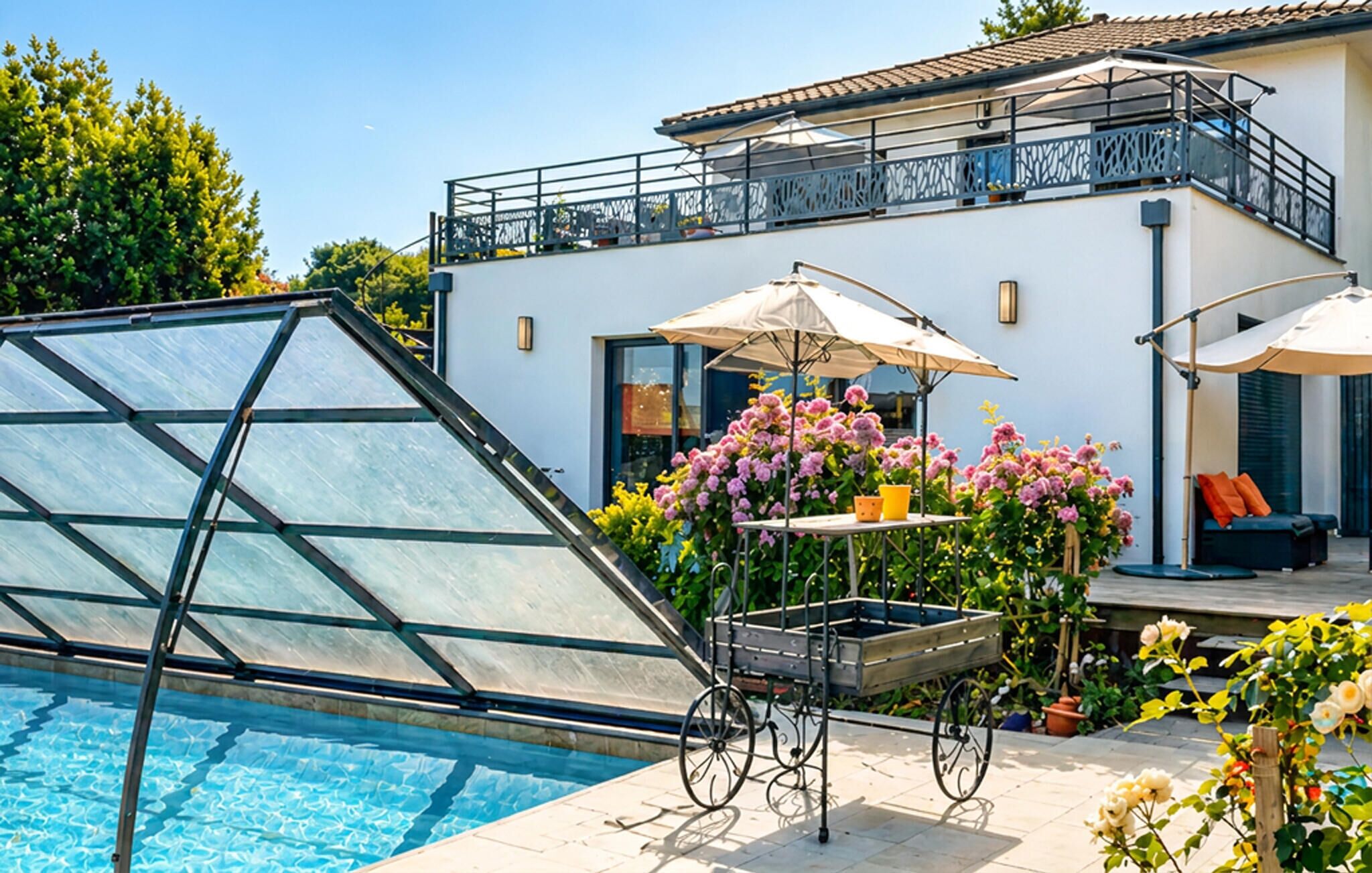 Een zwembadterras met een glazen constructie, een tafel met parasol en een bloemstuk.