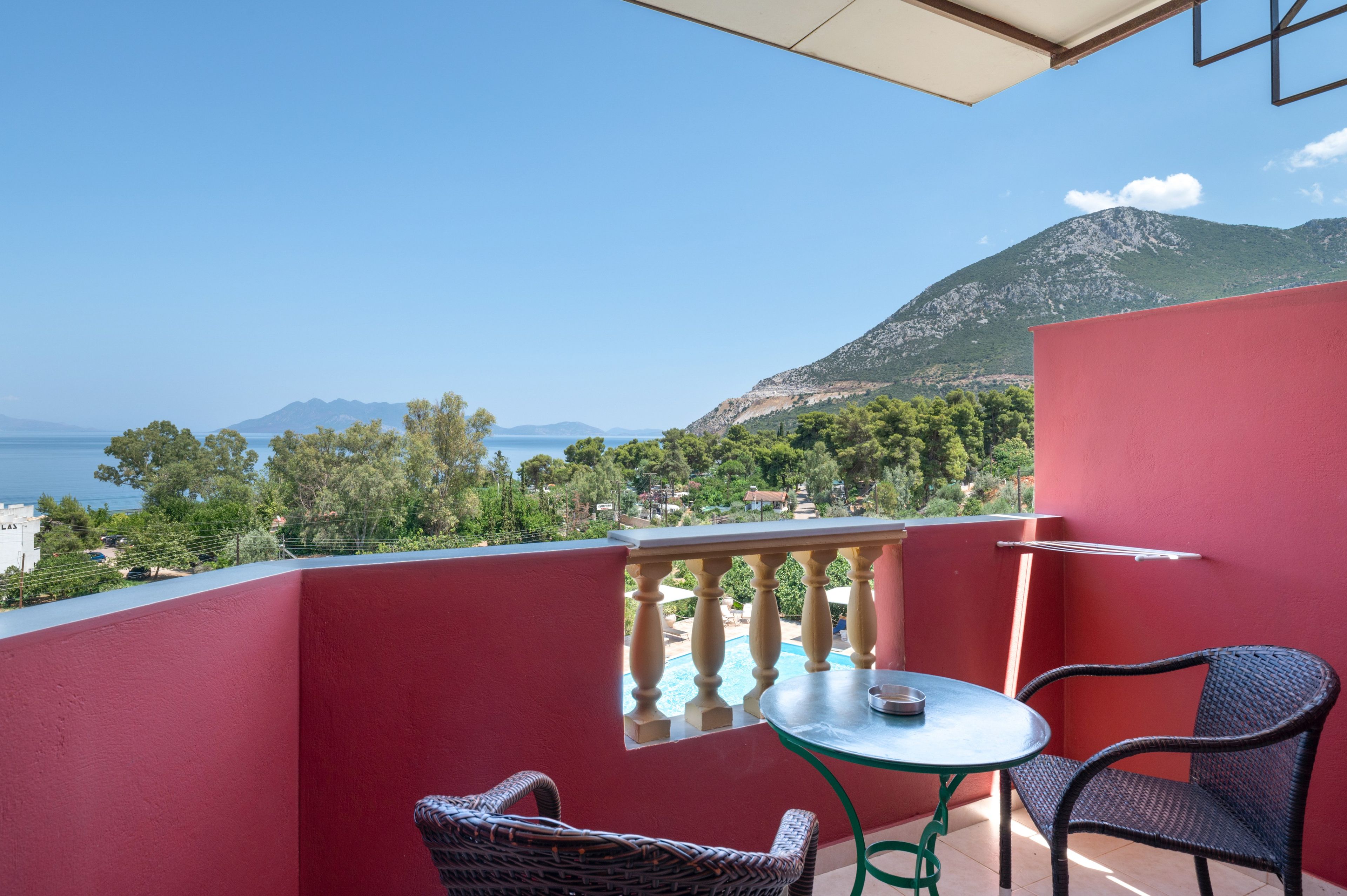Un balcon avec une table et des chaises, donnant sur un paysage montagneux et un plan d’eau.