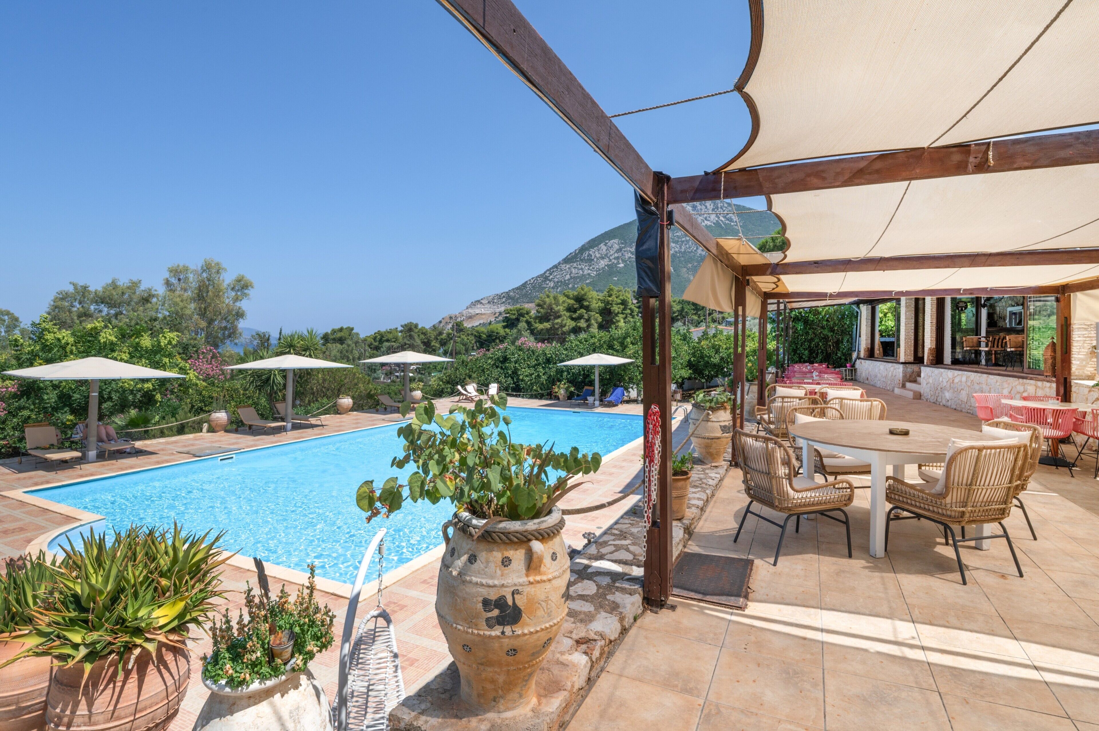 Un espace aménagé au bord de la piscine, comprenant un coin salon couvert, du mobilier d’extérieur et une vue sur une montagne.