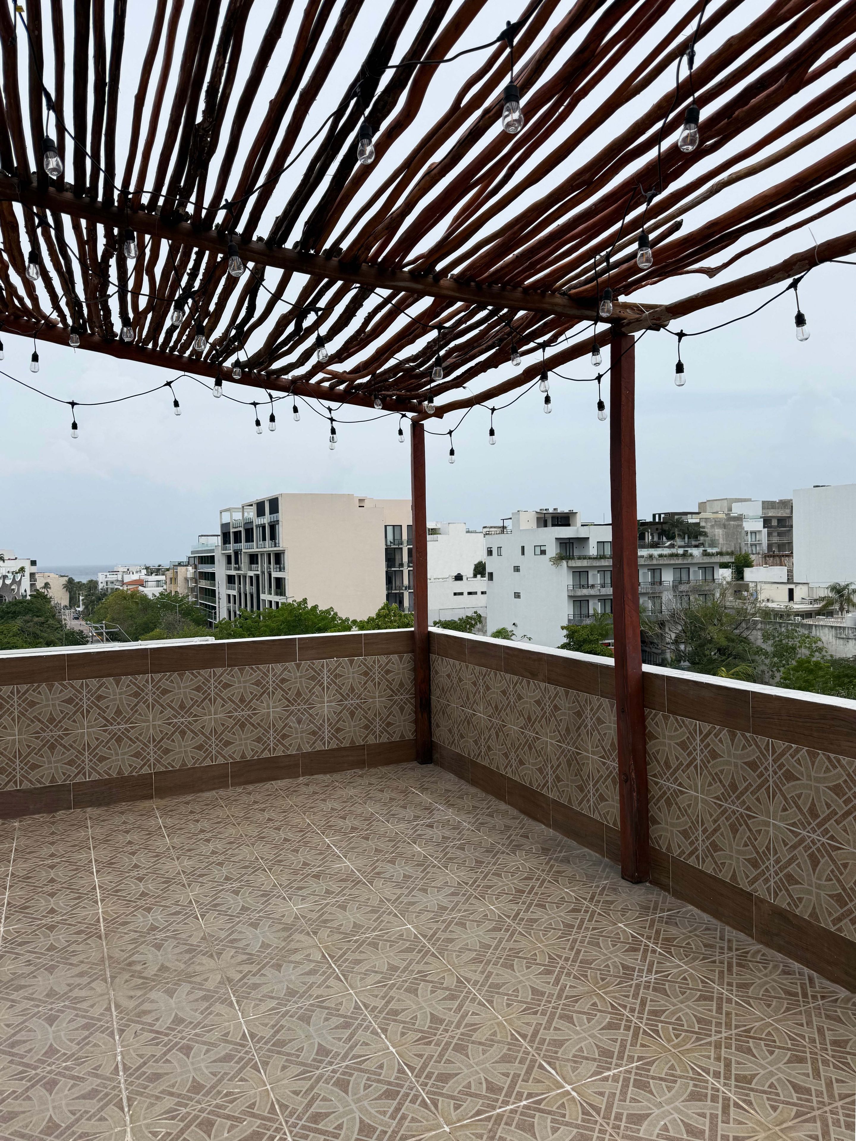 A covered outdoor area with a patterned floor, a wooden pergola, and string lights.