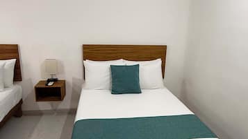 A single bed with a wooden headboard, white bedding, and a teal throw blanket. There is a nightstand with a lamp and a phone, and an air conditioning unit on the wall.