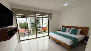 Een hotelkamer met een bed, een televisie en een balkon met uitzicht op gebouwen en bomen.