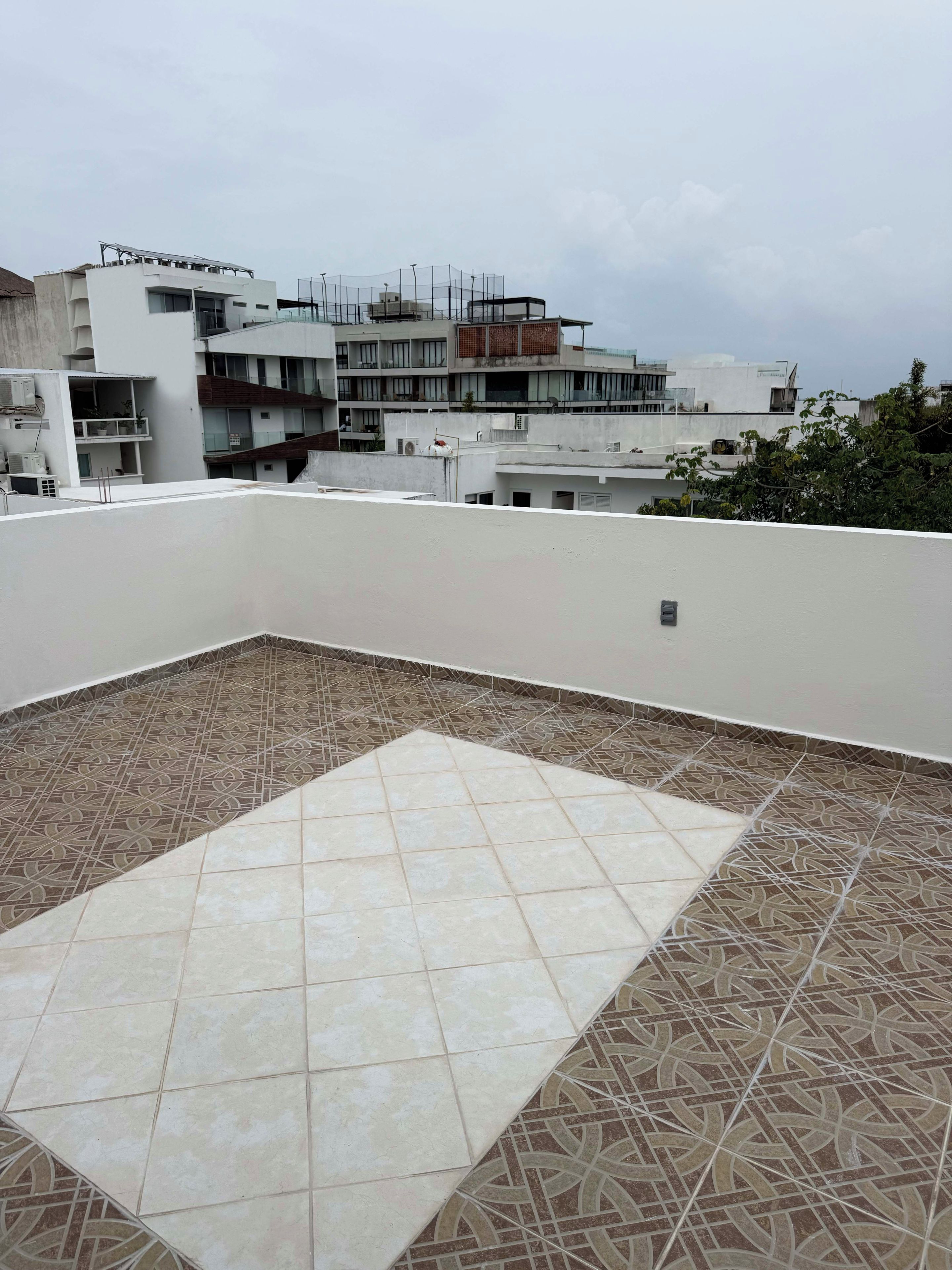 Una terraza en la azotea con baldosas estampadas, rodeada de edificios.