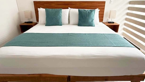 Een bed met een houten hoofdbord, wit beddengoed en twee teal-kleurige kussens.