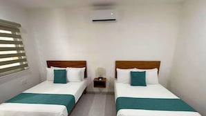 Een hotelkamer met twee enkele bedden, een nachtkastje met een lamp en een airconditioner aan de muur.