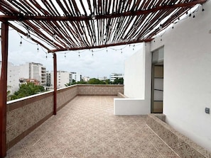 Terraço no telhado com piso estampado, pérgola de madeira e parede branca com porta.