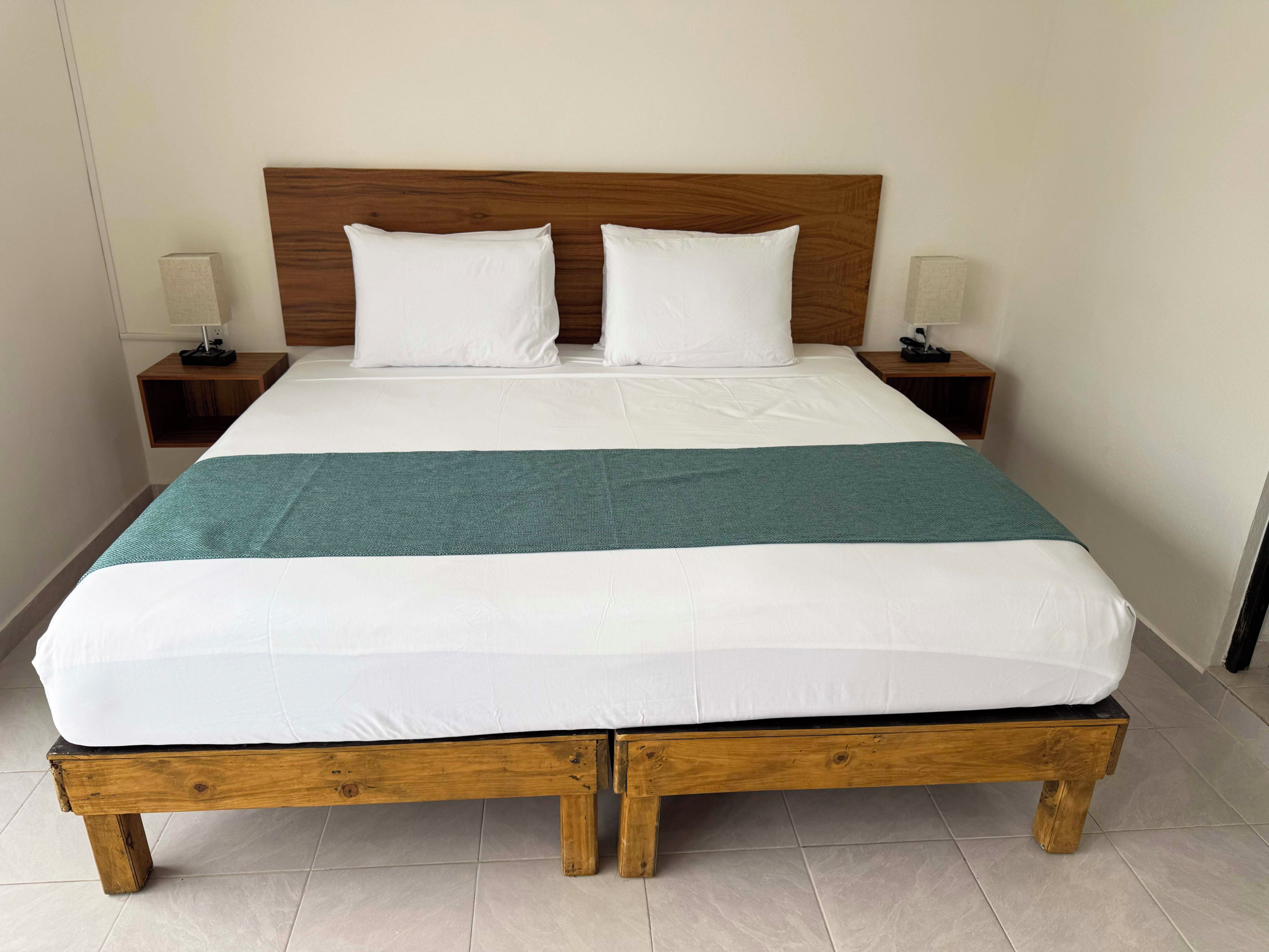 Ein Bett mit Holzrahmen, weißer Bettwäsche und einer türkisblauen Decke.