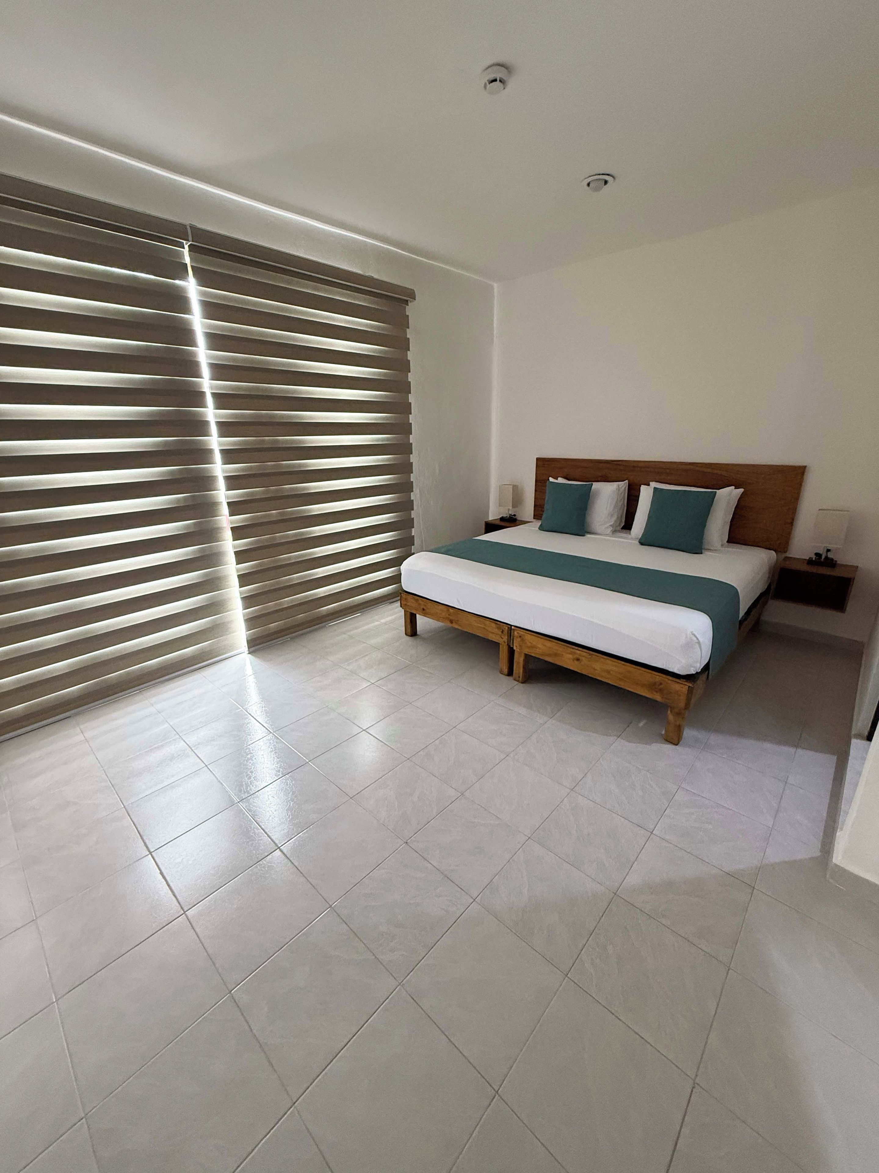 Une chambre d’hôtel avec un lit, une table de chevet et une fenêtre avec des stores.