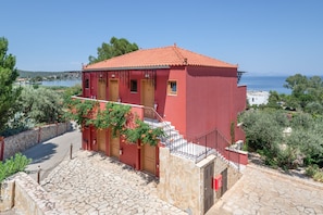 Un edificio rojo con una escalera de piedra que conduce a una puerta de madera, rodeado de vegetación y con vistas a una masa de agua.