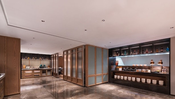 Un moderno vestíbulo de hotel con piso de mármol, armarios de madera y una zona de bar con botellas y vasos.