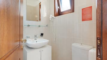Ein Badezimmer mit weißem Waschbecken, einem Spiegel, einer Glasablage, einer Toilette und einer Dusche.