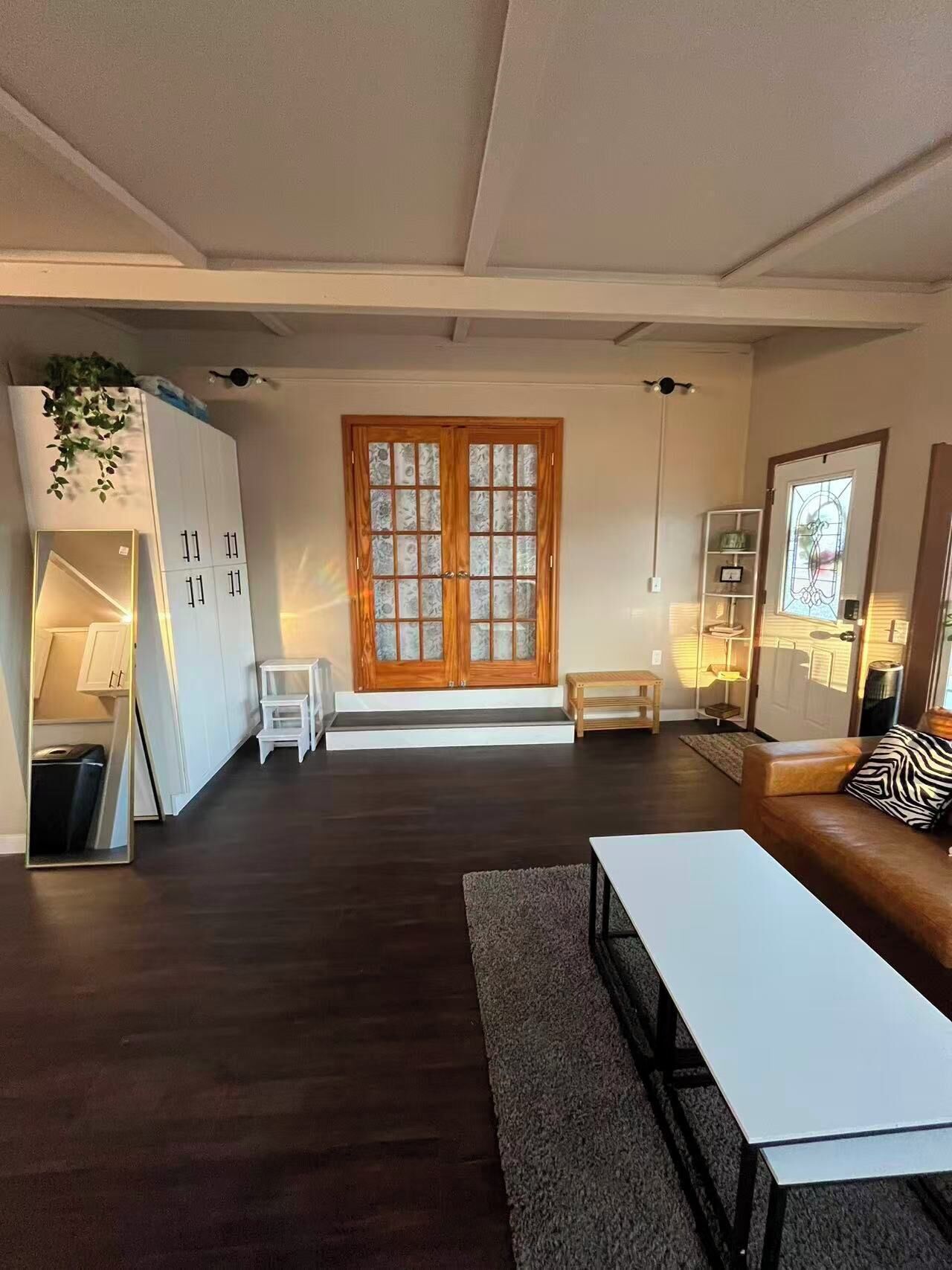 Ein modernes Wohnzimmer mit dunklem Holzboden, einem weißen Sofa, einem Couchtisch und einer großen Holztür mit Glasscheiben.