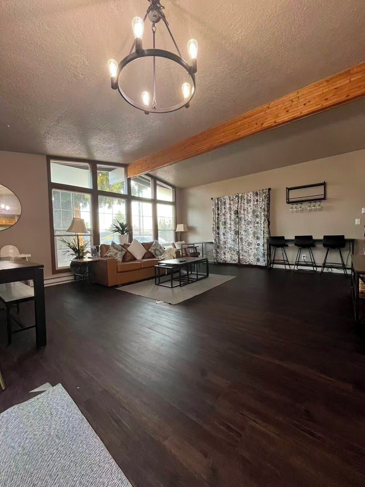 A spacious living area with a dark wood floor, a sofa set, a coffee table, and a chandelier.