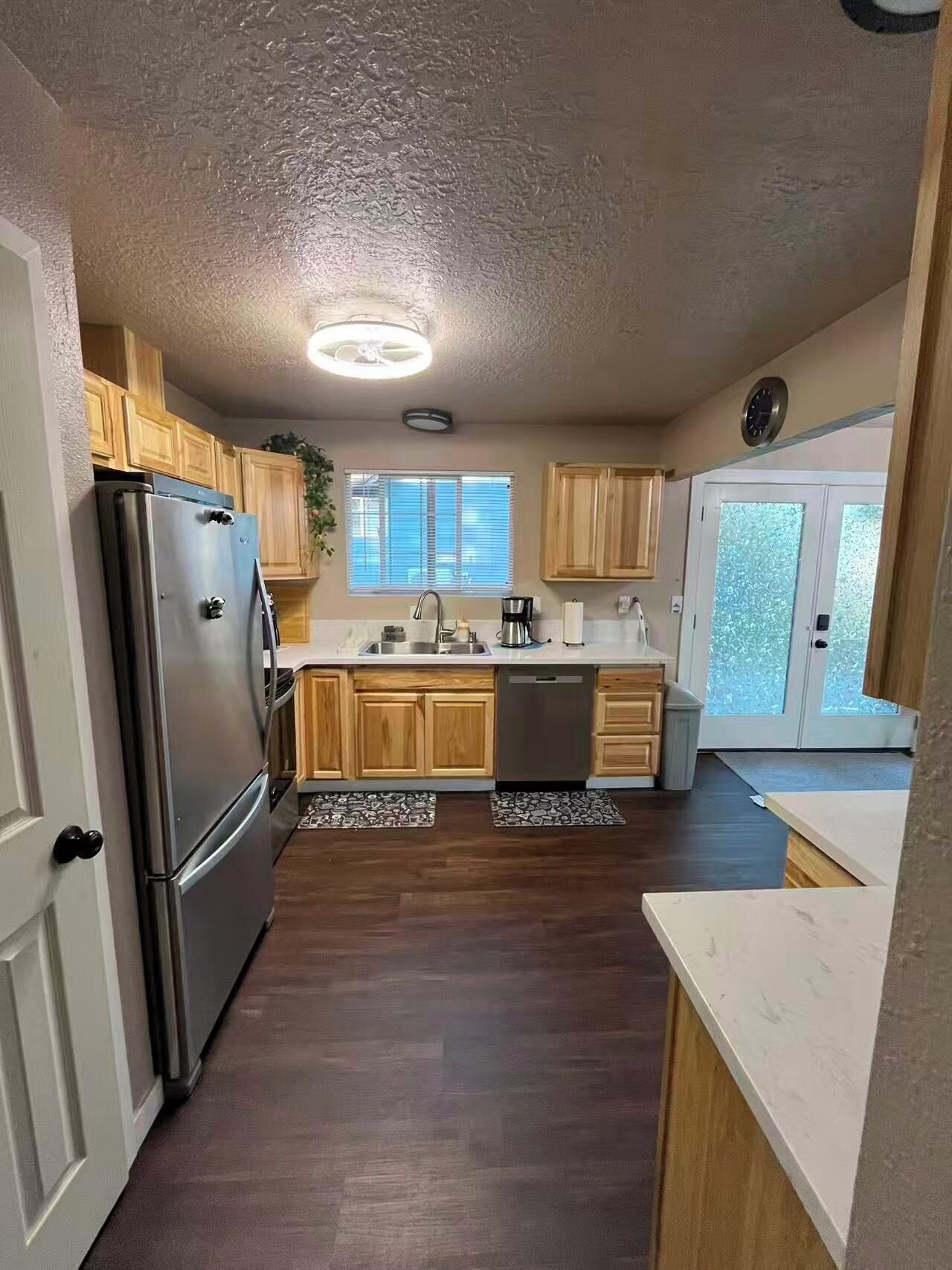 Eine Küche mit Holzschränken, einem Edelstahlkühlschrank, einem Geschirrspüler und einem Fenster mit Jalousien.