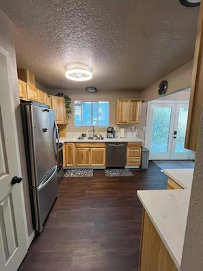 A kitchen with wooden cabinets, a stainless steel refrigerator, a dishwasher, and a window with blinds. - Quiet and spacious 4-bedroom 3-Bathroom house in Kelso, just minutes off I-5 (Kelso)
