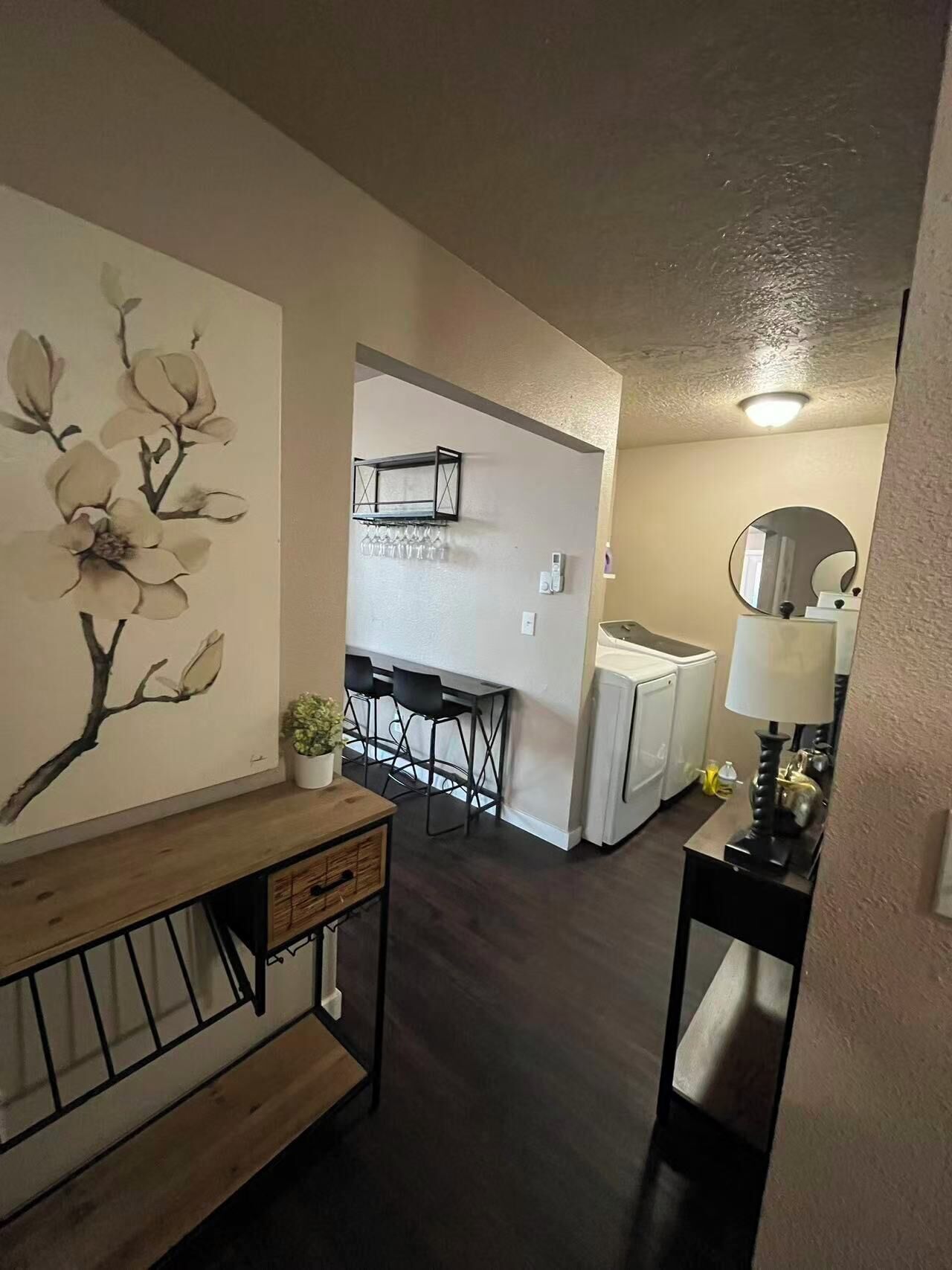 A modern kitchen with white appliances, a dining area with black chairs, and a wall-mounted shelf with glasses.