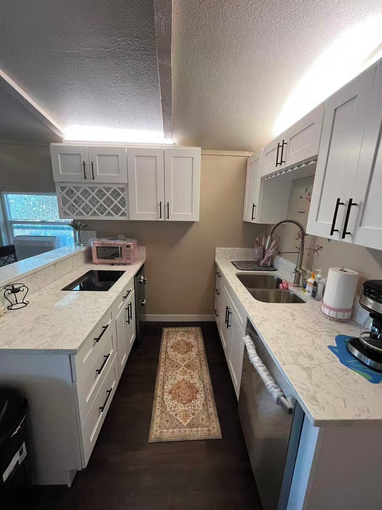 A compact kitchen with white cabinetry, a built-in microwave, a stainless steel sink, and a small rug.