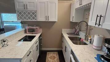 A compact kitchen with white cabinetry, a built-in microwave, a stainless steel sink, and a small rug.