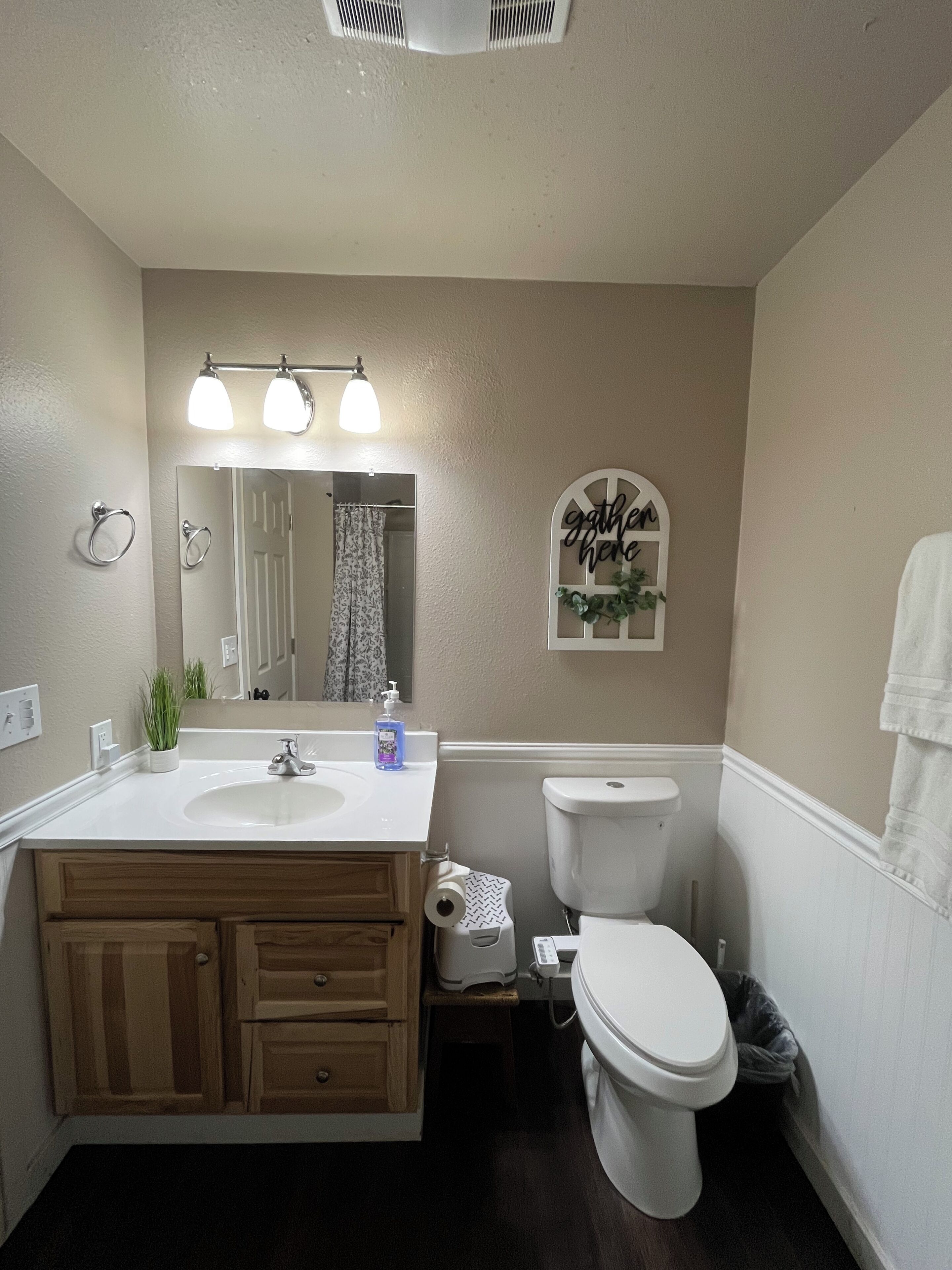 A bathroom with a double sink, a toilet, a mirror, and a wall-mounted light fixture.