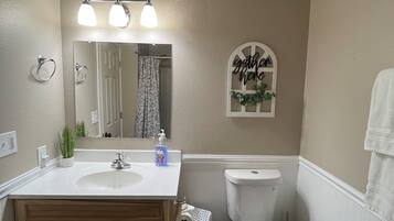 A bathroom with a double sink, a toilet, a mirror, and a wall-mounted light fixture.