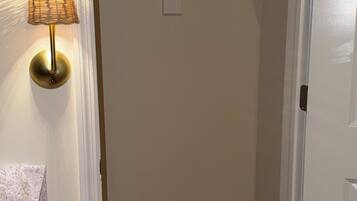 A bedroom with a bed, a bedside lamp, a closet with a hanging rod, and a door.
