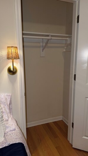 Ein Schlafzimmer mit einem Bett, einer Nachttischlampe, einem Kleiderschrank mit Kleiderstange und einer Tür.