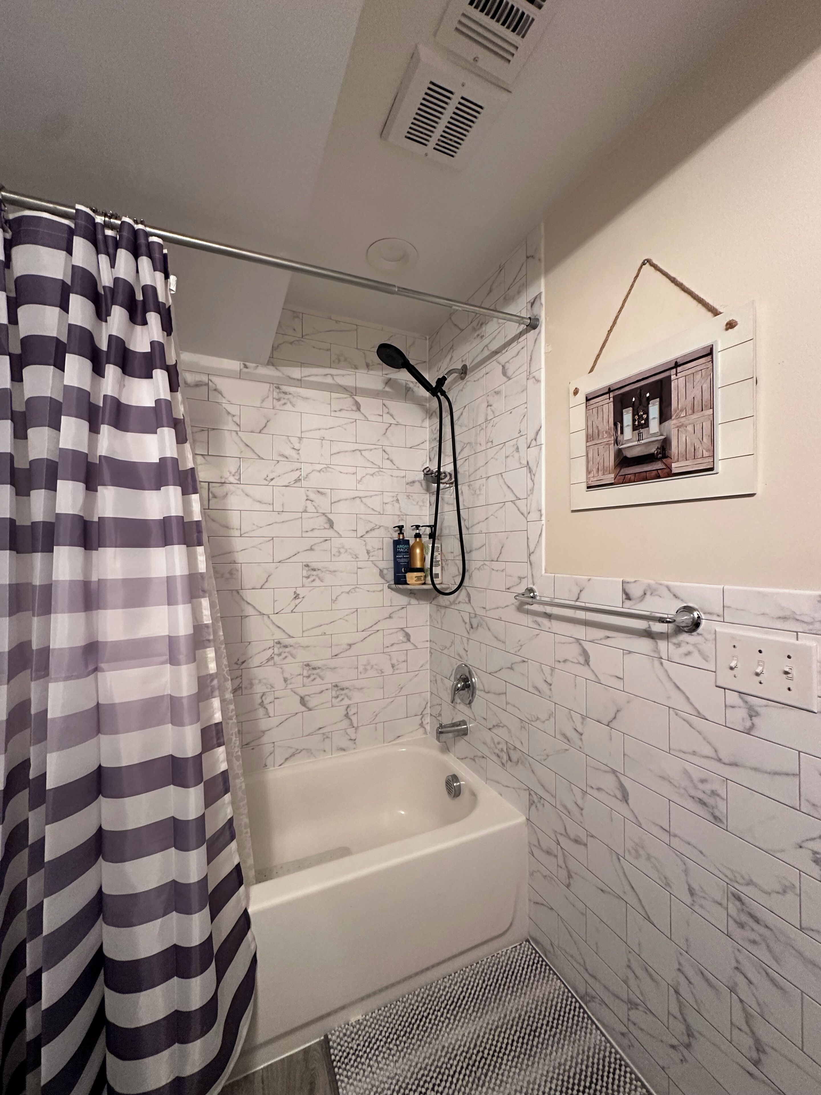 Ein Badezimmer mit einer Badewanne, einer Dusche, Marmorfliesen, einem gestreiften Duschvorhang und einem kleinen gerahmten Bild an der Wand.