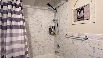 Ein Badezimmer mit einer Badewanne, einer Dusche, Marmorfliesen, einem gestreiften Duschvorhang und einem kleinen gerahmten Bild an der Wand.
