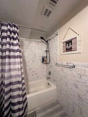 A bathroom with a bathtub, shower, marble tiles, a striped shower curtain, and a small framed picture on the wall.