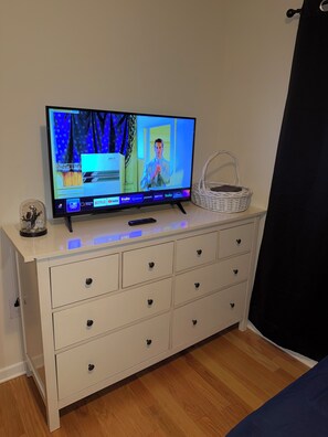 Une télévision posée sur une commode, avec une télécommande, un panier et un objet décoratif.