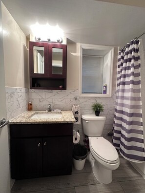Ein Badezimmer mit Marmorfliesen, einem Waschtisch, einer Toilette und einer Duschvorhang.