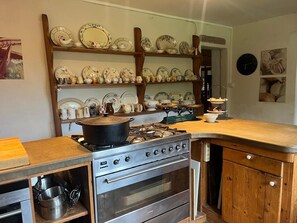 Una cocina con estufa, horno y estanterías llenas de vajilla.