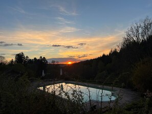 Une piscine entourée d’arbres, avec un coucher de soleil en arrière-plan.