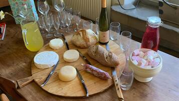 Une table en bois sur laquelle sont disposés divers aliments, notamment du fromage, du pain et une bouteille de vin, ainsi que plusieurs verres et une carafe contenant une boisson jaune.