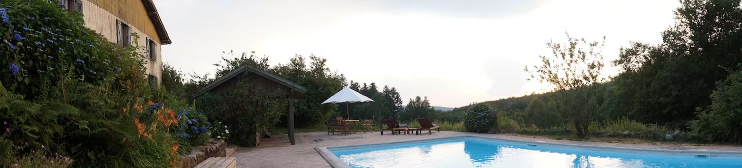 A swimming pool with a wooden deck, surrounded by lush greenery and a small gazebo.