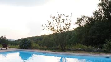 A swimming pool with a wooden deck, surrounded by lush greenery and a small gazebo.
