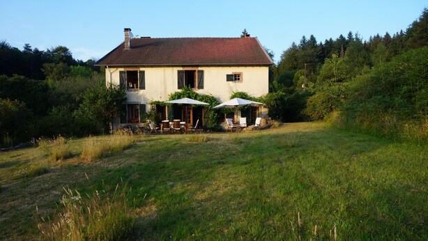 A two-story house with a sloped roof, surrounded by a grassy field and dense forest. - Holiday Home "Harmangouty": Private Pool, 2.5 ha Grounds & Tranquil Forest Retreat (Raon-aux-Bois)