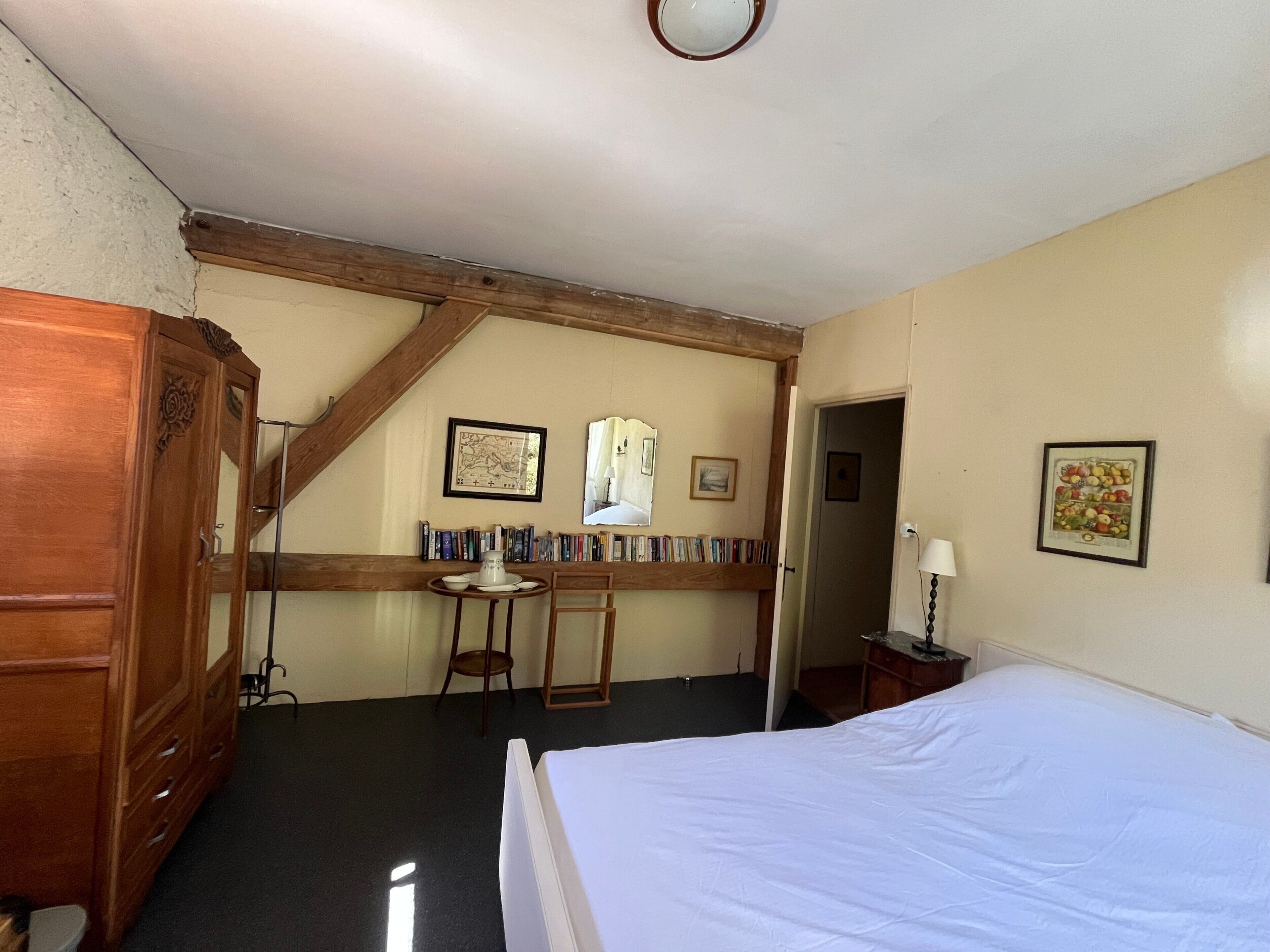 Quarto com cama, guarda-roupa de madeira, escrivaninha com livros e quadro na parede.
